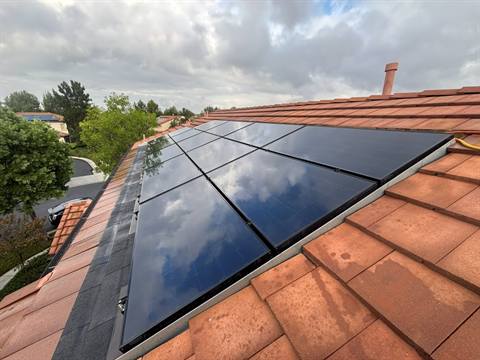 Clean all-black solar panels on a red clay tile roof, reflecting the clouds overhead