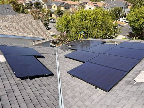 Two sections of freshly cleaned solar panels on a shingle roof above a tree-lined street