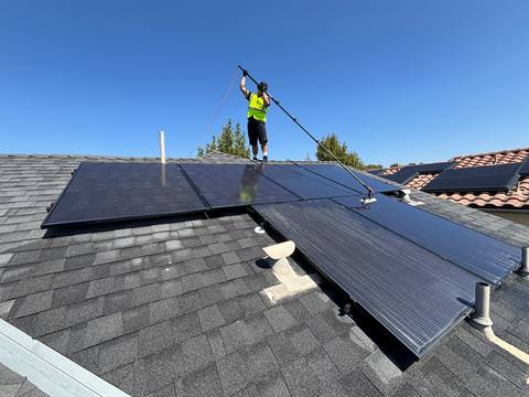 A Nano Solar Clean technician in a high-visibility vest cleaning rooftop panels with a water-fed pole and soft brush