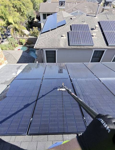 Water-fed pole mid-clean on a real Nano Solar Clean job: rinsed panels in front shine while the ones behind are still dusty
