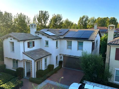Two-story white stucco home with a tile roof and a full array of black solar panels
